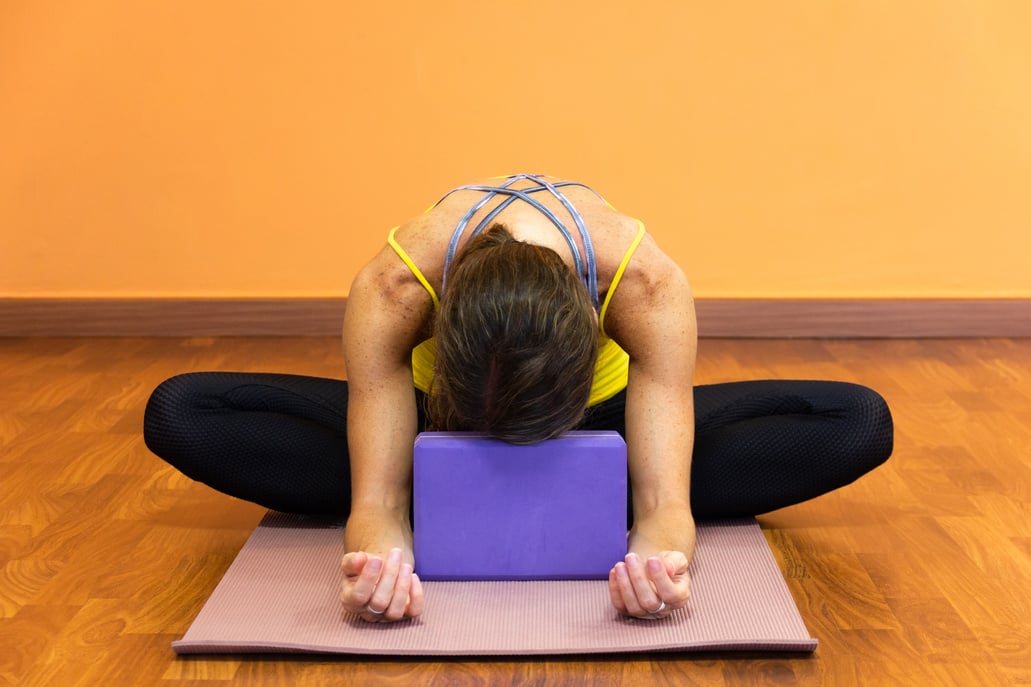 Woman in butterfly yin yoga asana with forehead resting on purple prop